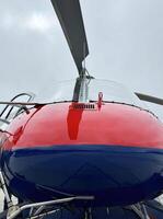 Red and blue helicopter close-up with rotor blades against cloudy sky photo