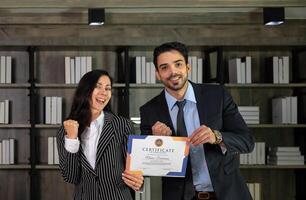 Portrait of two caucasian business woman and man in formal wear holding a certificate of appreciation recieved from business performace competition award winning in modern office photo