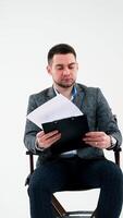 Serious businessman holding a folder and reading documents. Paper works flying over the handsome man in grey suit isolated on white studio background. Vertical video