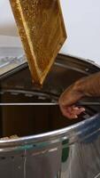 Apiarist inserts the honey wooden frame into metal barrel centrifuge. Loading the honey extractor device at apiary for harvesting honey. Vertical video