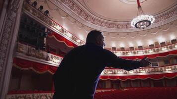 Man talking on a scene of a large theatre. Actor practising on stage before the performance in empty auditorium. Back view. video