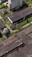 Rusty destroyed roofs of abandoned factory buildings. Empty ruined territory of a factory in spring. Aerial view. Vertical video