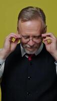 Portrait of a handsome grey-haired man. Mature man taking off his eyeglasses with a smile and looking at camera on yellow background. Vertical video