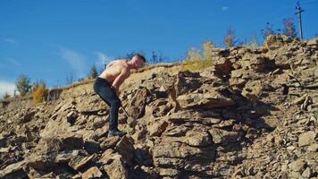 Side view of a strong man breaking stones with a hammer. Shirtless athletic man exercising with a sledgehammer on the rocky background. Slow motion. video