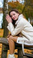 relajado calma pelinegro dama se sienta en el mesa pensando de algo. caucásico niña disfrutando hermosa otoño día en el parque entre abedul arboles vertical video