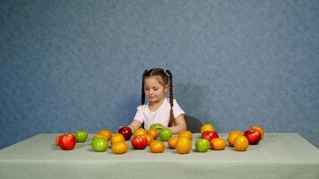Cheerful little girl playing with ripe fruits on the table. Happy child building a tower with fresh organic apples. Healthy fruits full of vitamins on the table. video