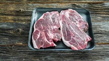 Two raw lamb shoulder chops on black styrofoam tray against weathered wood background photo