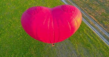 Large aerostat in the air. Beautiful red hot air balloon in the heart shape flying in the countryside. People travel in the basket of the airship in summer. Close-up. video