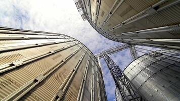 Grain elevators under blue sky. Huge metal grain storage tanks. Silver containers. Close-up. View from below. video