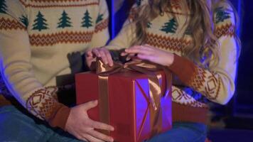 Couple in Christmas sweaters with a box gift. Woman unties ribbon from the present box. Romantic atmosphere during New year celebration. Close-up. video