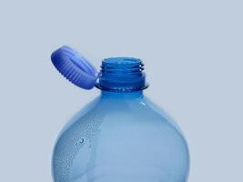 A new mechanism of plastic bottle with a stationary fixed tethered cap. Blue plastic PET water bottle with cup open close up isolated on white. Recycling, environment friendly and ecology concept photo