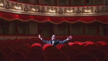 Successful man in suit alone in large auditorium. Actor man is sitting among empty red armchairs and singing in opera house. video