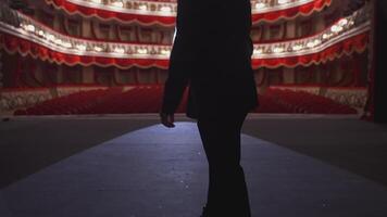 Man with microphone on theatre stage. Male actor in elegant suit walks on scene and starts speech in front of the empty auditorium. Back view. video