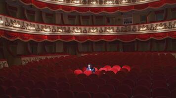 Rich man in mask in empty theater hall. Man spectator is sitting alone in large auditorium and looking to the sides. Consequences of pandemic. video