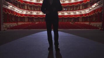 Man in suit standing on stage back to auditorium. Dark silhouette of unrecognizable actor on the background of classic theatre hall in red and white colors. video