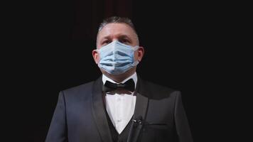 Man in elegant suit and medical mask. Portrait of an actor in protective facial mask standing on stage of a theater. Man putting off mask from face. Coronavirus pandemic. video