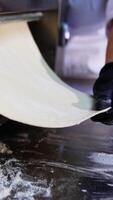 Food factory worker pulls the layer of dough from a roller machine. Fresh pastry dough is laid on the metal table surface. Vertical video