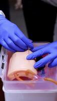 Hands in gloves doing injection on a dummy arm. Practitioner learning to with a syringe into a mannequin hand. Close-up. Vertical video