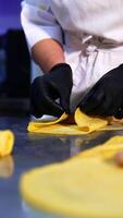Careful hands of cook in gloves roll minced meat into a thin pancake. Ready-made crepes with stuffing at foreground. Close up. Vertical video