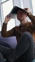 Tired businessman with a laptop on his head. Man is sitting in the office by the large window and holding a laptop over the head. Problems in business. Vertical video