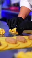 Preparing the crepes stuffed with fried minced meat. Factory worker rolling the stuffing into a yellow thin pancakes. Blurred foreground. Vertical video