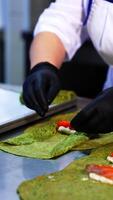 Unusual green crepes are rolled with cheese and salmon fish. The cook rolls the pancakes and lays them on the tray. Close up. Vertical video