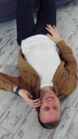 Young man talking the phone at home. Happy man having a conversation through the phone while lying on floor near the sofa. Top view. Quarantine. Vertical video