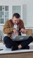 Young man pressing buttons on a laptop at home. Funny face of a businessman after working long hours on a computer. Tired mad man on the table at home with a laptop. Vertical video