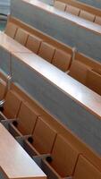 Modern desks in lecture hall. Rows of long wooden tables with vacant seats in the light auditorium at university. Classroom without students. Vertical video