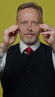 Senior man holding eyeglasses in front of himself. Magnifying glasses in man's hands showing big funny eyes of an old man. Slow motion. Vertical video