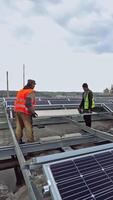 Engineers carry solar panel on a solar farm. Two workers installing blue sunny battery on a metal basis on a rooftop. Clean environmental energy from the sun. Vertical video