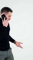 Handsome man having phone talk indoors. Serious young businessman talking on a cellphone and moves slowly isolated on white background. Slow motion. Vertical video