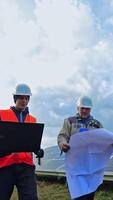 Workers in hard hat on the solar farm. Engineers talk about solar panels installation. Technicians with a laptop and project discuss the construction of new ecological station. Vertical video