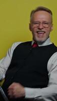 Funny elderly man dancing with a mop. Amusing old man in suit singing happily with a stick like playing the guitar on yellow background. Positive emotions. Vertical video