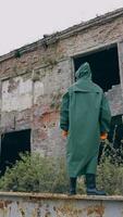 Man in protective clothes in abandoned place. Man in safety suit standing alone on the background of ruined buildings. No people. Apocalypse concept. Vertical video