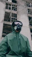 Portrait of a man in safety suit in radiation zone. Person in gas mask and protective uniform standing alone on ruined building background. Apocalypse concept. Vertical video