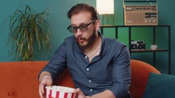 Lebanese man sits on couch eating popcorn, watching interesting TV serial sport game online at home video
