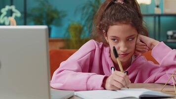 Bored tired school girl doing homework exercise online, typing on laptop makes notes in notebook video