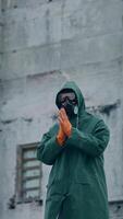 Man in protective suit and mask in infected zone. Person wearing respirator and safety uniform, in protective gloves standing on the background of abandoned building. Vertical video