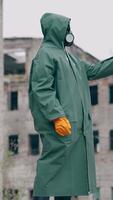 Human in a protective suit and gas mask with a phone. Unrecognizable person in safety uniform, gloves and respirator doing selfie in the destroyed place during radiation. Vertical video