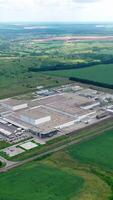 Factory on green landscape. Large industrial territory surrounded by green fields and forests. Manufacturing among nature. Aerial view. Vertical video