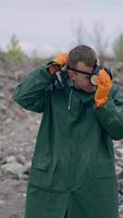 Ecologist puts on respirator in abandoned place. Man in protective suit protects himself with a gas mask in radioactive zone. Chemical attack. Vertical video