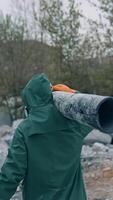 Man in safety suit walking in dangerous zone. Human in protective uniform and respirator is carrying pipe in the abandoned place with polluted air. Rear view. Vertical video