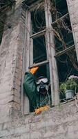 Ecologist wearing respirator alone in empty house. Man in safety suit and mask looking out of the window without glass from abandoned building. Chemical attack. Vertical video
