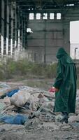 Man in protective suit and respirator in abandoned building. Ecologist in safety suit near the pile of garbage in the ruined place. Radiative zone. Vertical video