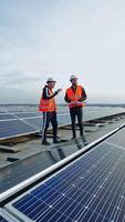 Modern solar farm on a roof under the sky. Workers in uniform and protective helmets discuss the solar panels installation. Vertical video