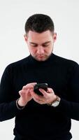 Serious man touching the screen of smartphone indoors. Bearded businessman holding a modern gadget in his hands and working on it in empty studio. Vertical video