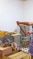 Light room with wooden hives and boxes in it. Male apiculturist replaces honey frames from one box to another. Vertical video
