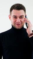 Portrait of a smiling man talking on the phone. Handsome businessman in black sweater talking on a mobile phone isolated in white studio. Vertical video