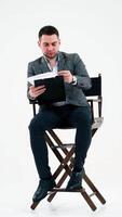 Elegant man with a folder. Businessman sitting on the chair and reading documents. Many papers are flying in the studio over the handsome man. Vertical video